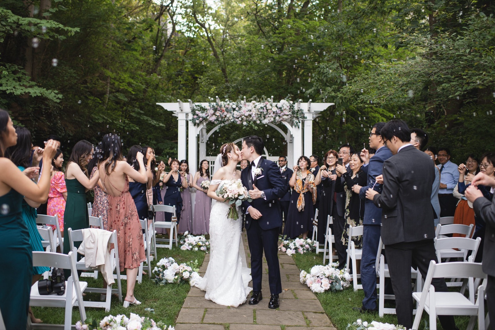 Guests cheer as a couple kisses at the end of the aisle.