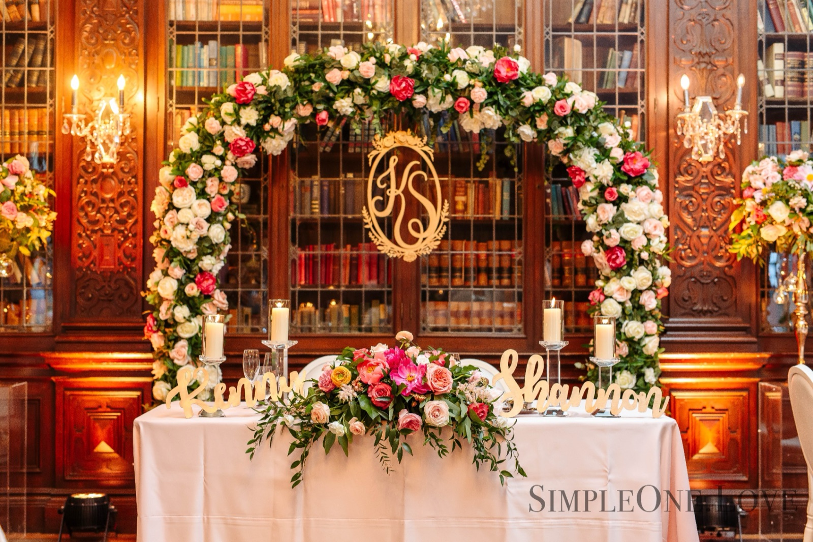 A floral arch and head table in front of Casa Loma's library shelves.