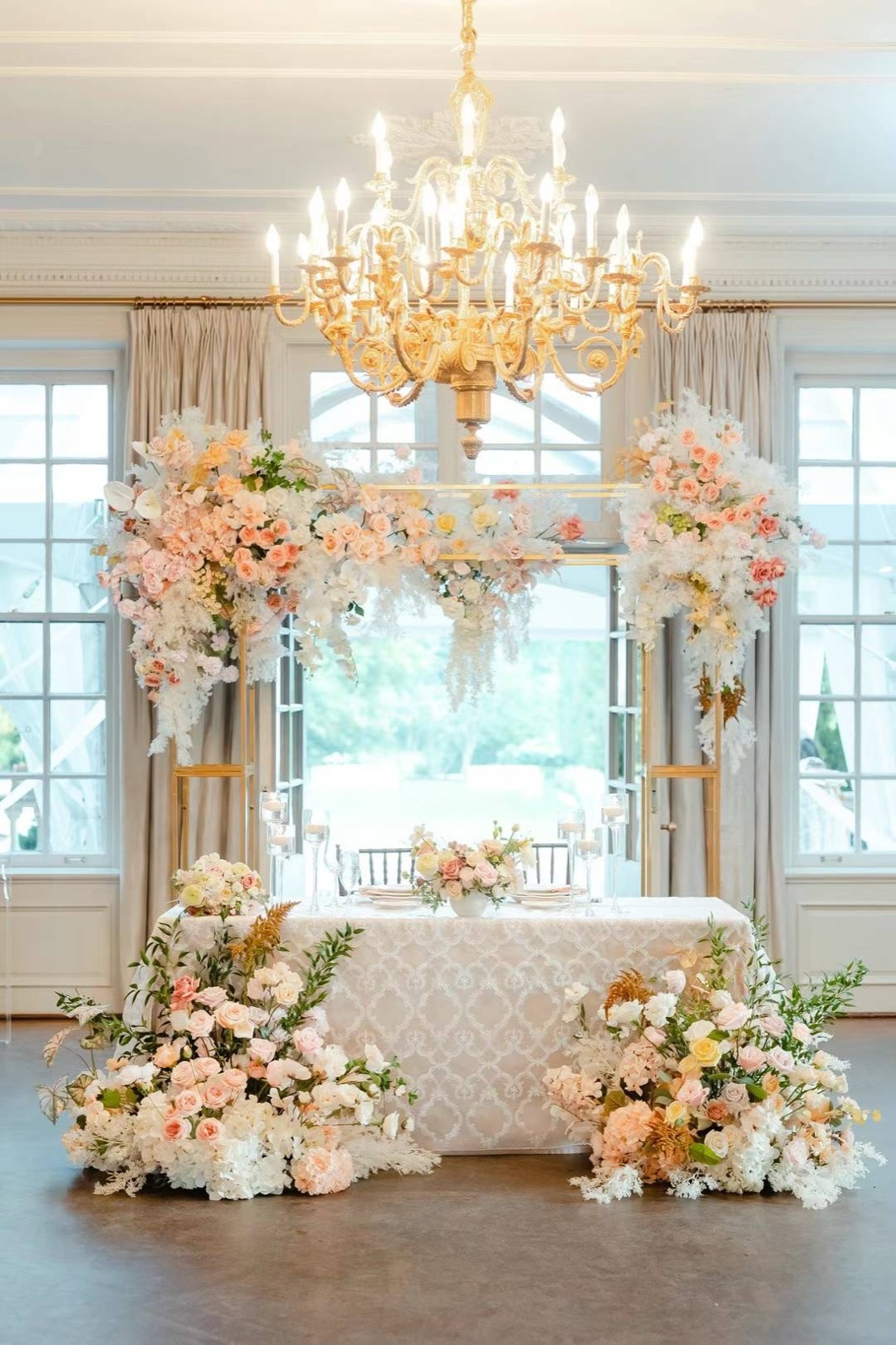 A sweetheart table beneath a chandelier and tall windows.
