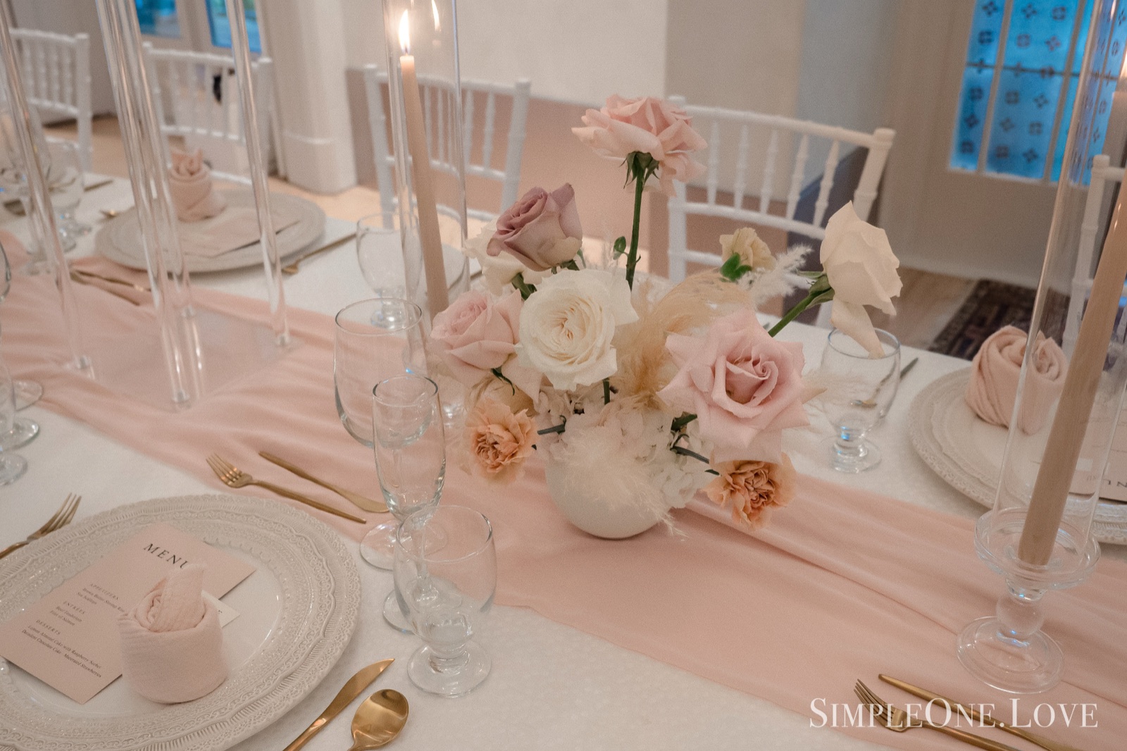 Blush roses, a silk runner and glassware on a set table.