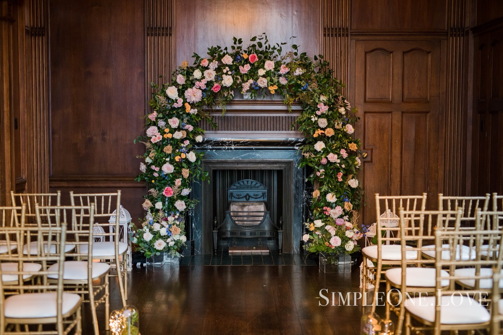 A flower arch built around a carved fireplace, chairs set for the ceremony.