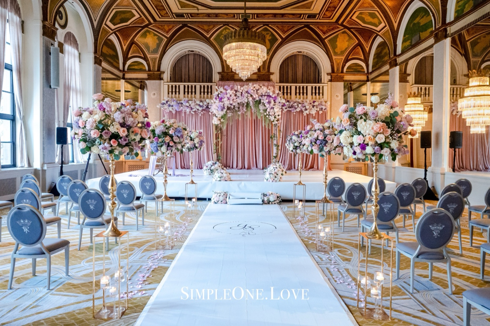 An indoor ceremony aisle under a painted, gilded ceiling.