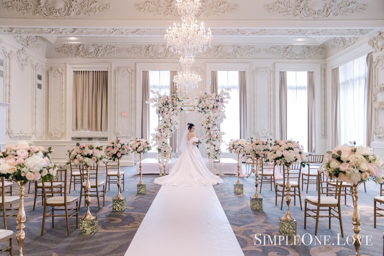 A bride on the aisle of a ballroom set for the ceremony.