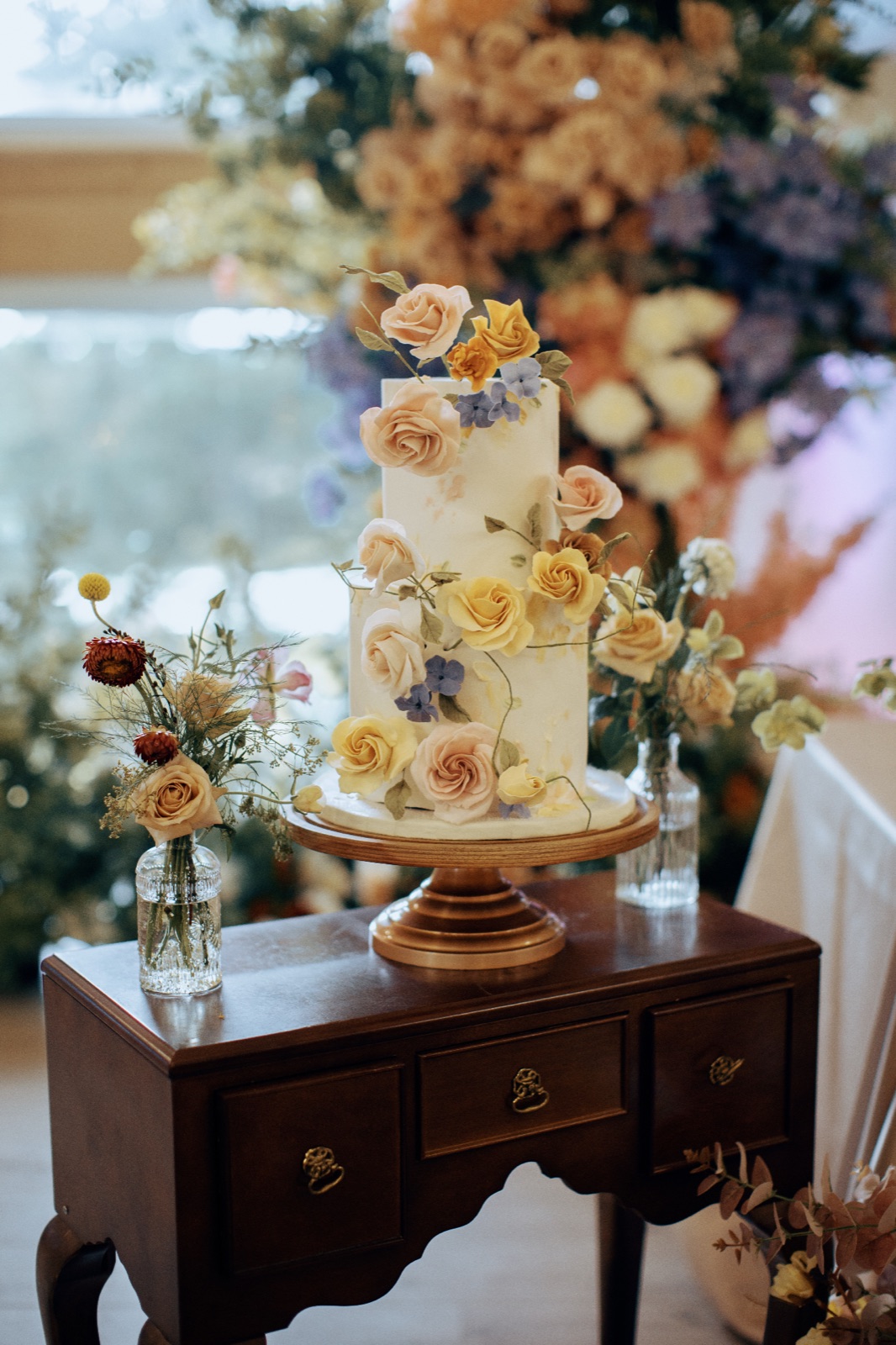 A cake decorated with sugar flowers on an antique side table.
