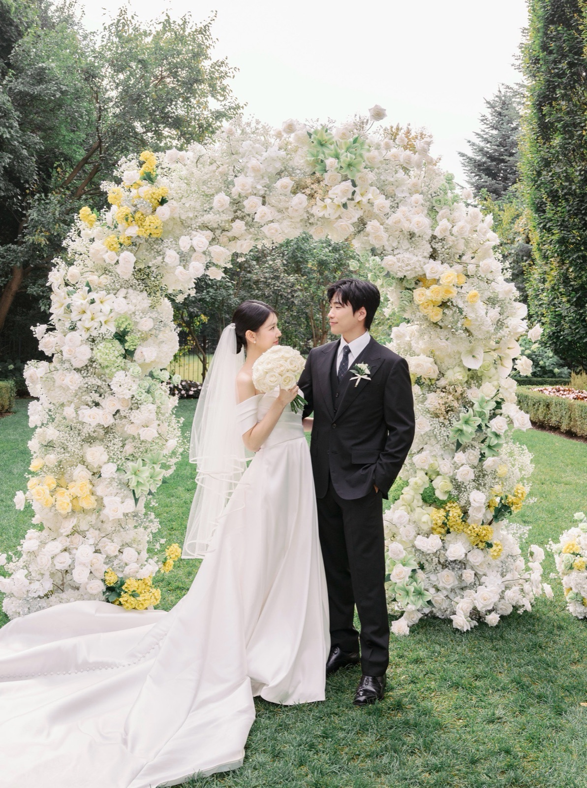 A couple under a garden arch of white flowers.