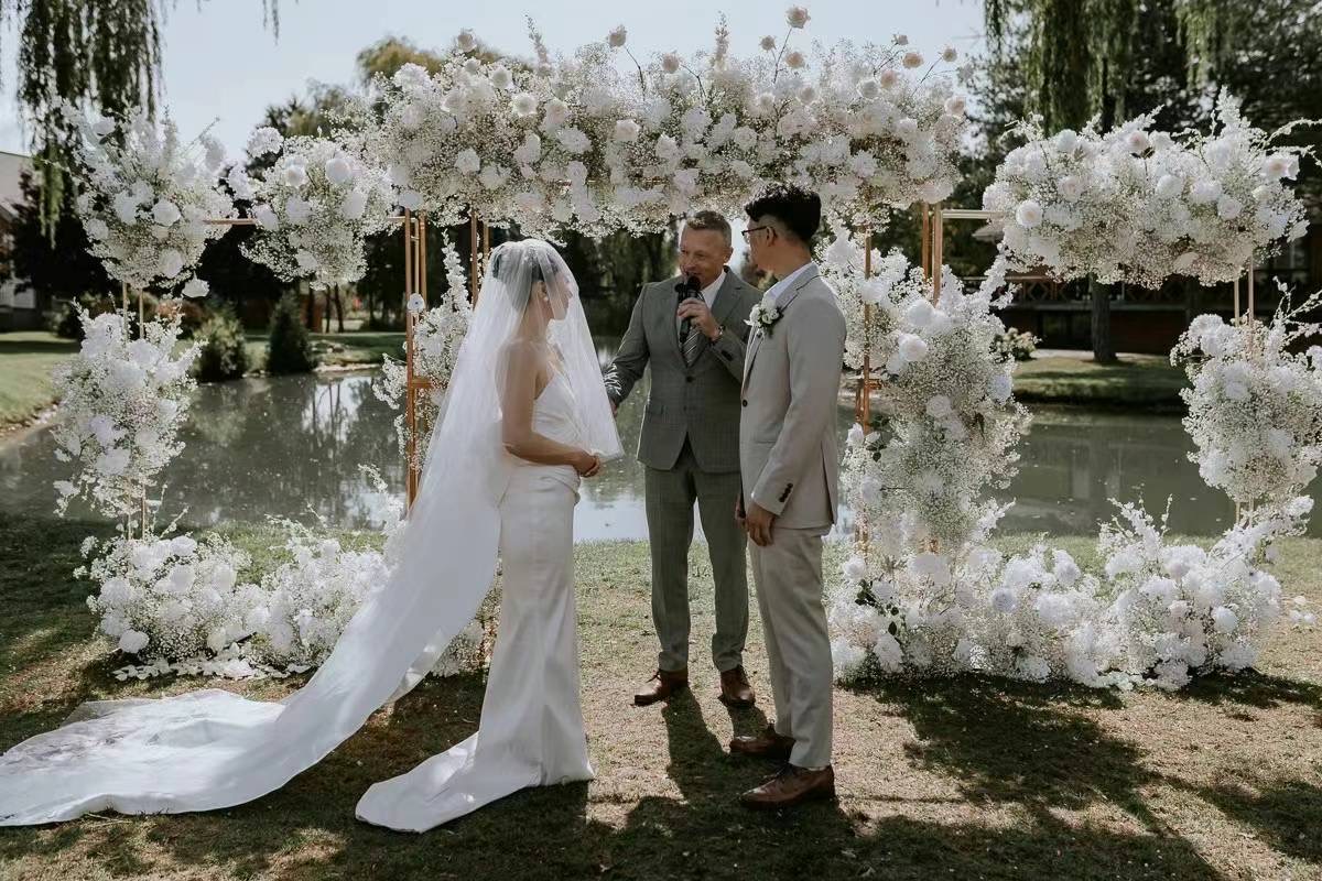 A couple and their officiant among white flowers outdoors.