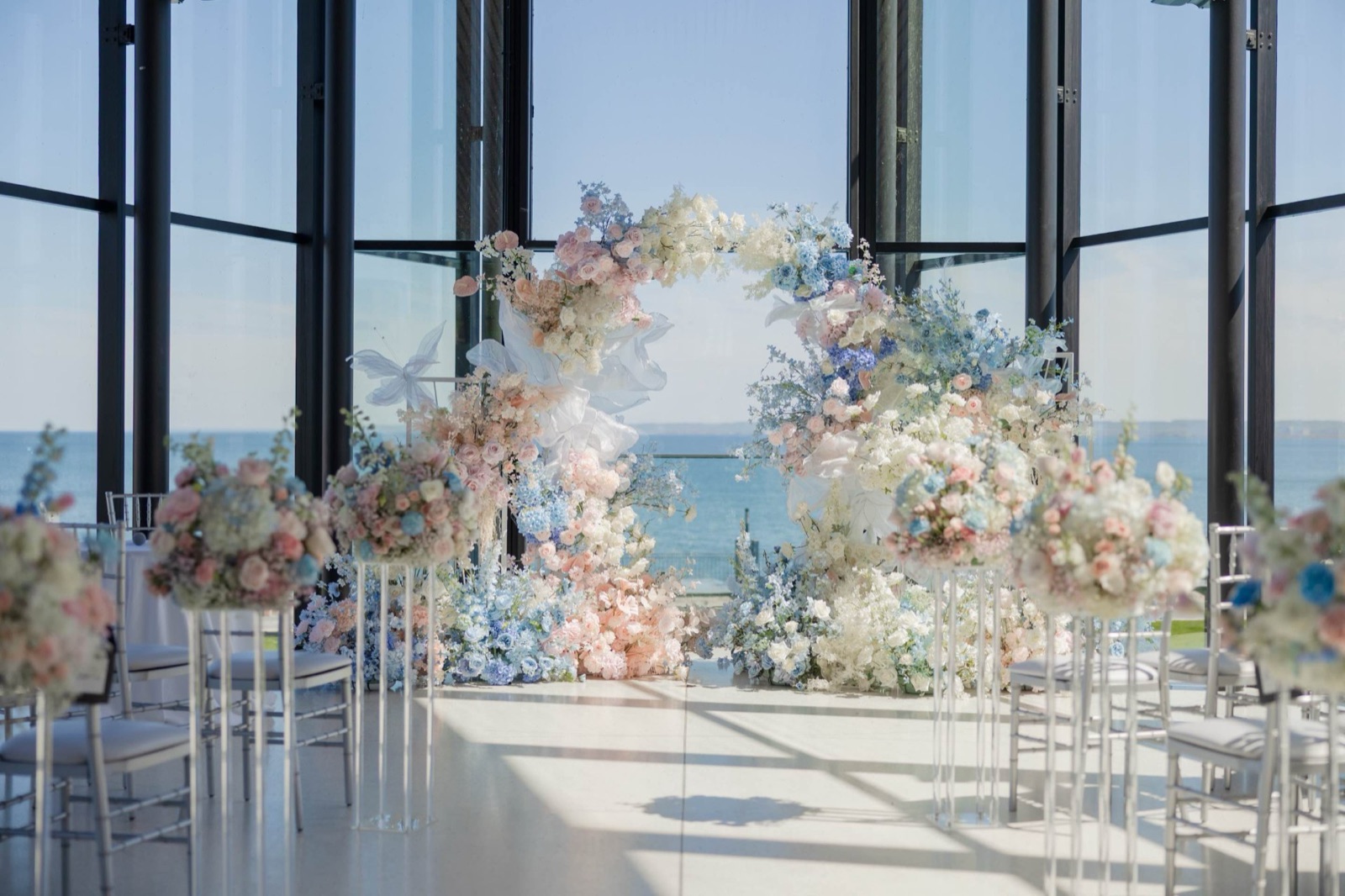 A glass-walled room above the lake, chairs set before a flower arch.