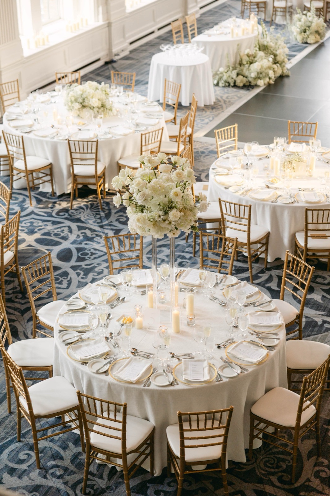 Round tables with gold chairs on a patterned ballroom carpet.