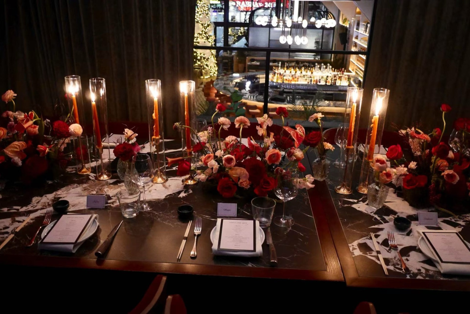 A candlelit table of red flowers in a dark room.